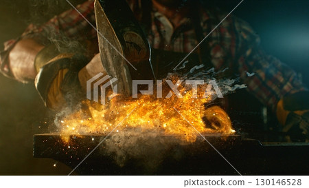 The blacksmith manually forging the molten metal on the anvil in smithy with spark fireworks 130146528