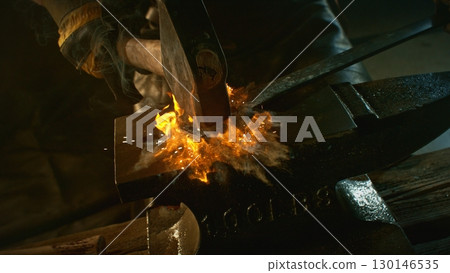 The blacksmith manually forging the molten metal on the anvil in smithy with spark fireworks The blacksmith manually forging the molten metal on the anvil in smithy with spark fireworks 130146535