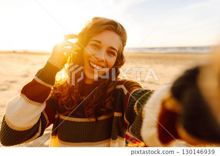 Young woman taking a cheerful selfie on a sandy beach during sunset. Lifestyle, travel, active life Young woman taking a cheerful selfie on a sandy beach during sunset. Lifestyle, travel, active life 130146939
