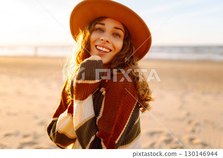 Young woman enjoying sunset at beach while wearing cozy striped sweater. Relax and lifestyle concept 130146944