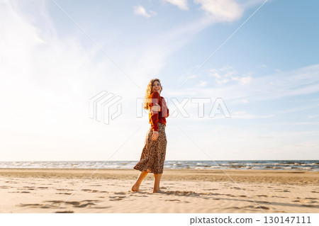Stylish woman walks at sunset along beach of sea on at sunset. Travel, relax and lifestyle concept. 130147111