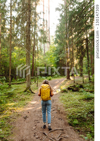 Tourist woman hiking alone in thick autumn forest. Stylish female looks for pathway among trees. Tourist woman hiking alone in thick autumn forest. Stylish female looks for pathway among trees. 130147309