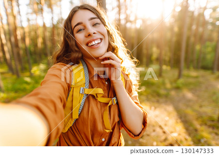 Beautiful woman taking picture of herself while walking in sunny forest. Selfie in nature. Adventure Beautiful woman taking picture of herself while walking in sunny forest. Selfie in nature. Adventure 130147333