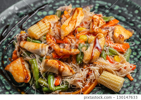 Stir fried rice noodles with chicken and vegetables served on a plate 130147633