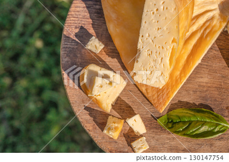 Sliced smoked cheese with small cubes and basil on wooden board 130147754