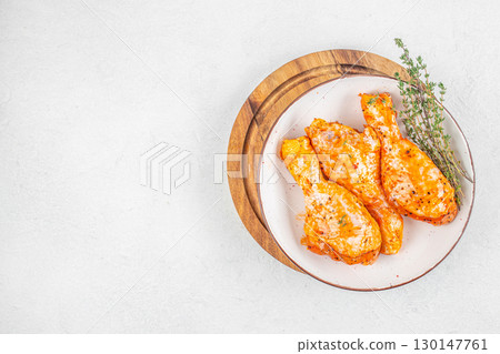 Raw marinated chicken drumsticks with spices and herbs on white plate. top view. copy space Raw marinated chicken drumsticks with spices and herbs on white plate. top view. copy space 130147761