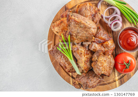Grilled pork pieces served with onion rings and tomato sauce on wooden plate. top view. copy space 130147769