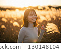 A woman bathed in light in a field of silver grass at sunset 130148104