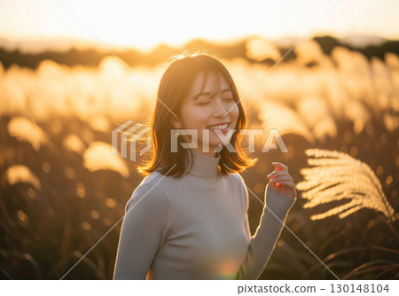 A woman bathed in light in a field of silver grass at sunset 130148104