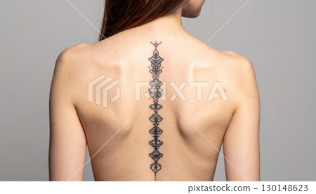 Detailed Geometric Spine Tattoo on Woman's Back with Smooth Skin on Grey Backdrop 130148623