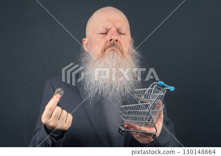 Elderly Man Examining a Coin Next to a Small Shopping Cart. Symbolizing Budgeting and Spending Elderly Man Examining a Coin Next to a Small Shopping Cart. Symbolizing Budgeting and Spending 130148664