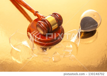 A wooden gavel with a gold band rests on a base beside a shattered hourglass 130148702