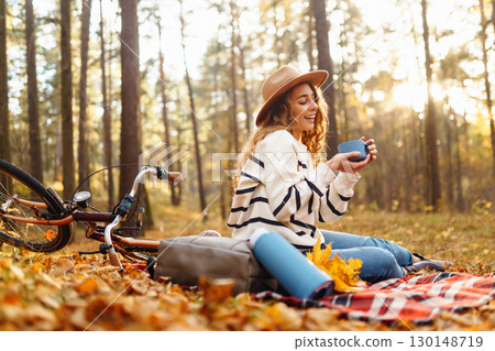 Relax in forest Woman sits on blanket, drinks from thermos, enjoys autumn atmosphere in sunny forest 130148719