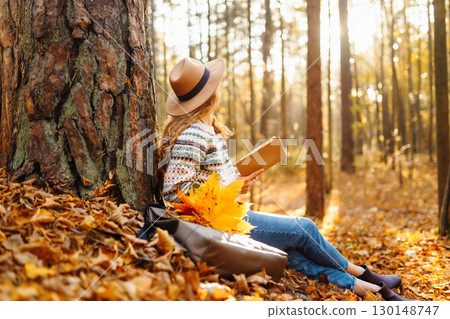 Stylish woman reading a book in the autumn park. Relaxation, enjoying, solitude with nature. 130148747