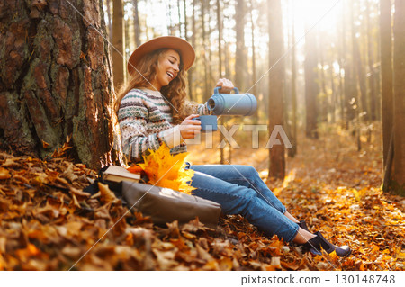 Cute young woman drinks hot drink from thermos and enjoys nature. Autumn landscape. relax concept. 130148748