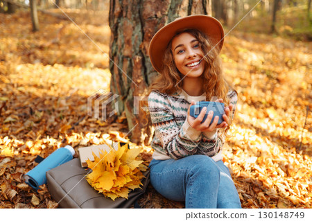 Cute young woman drinks hot drink from thermos and enjoys nature. Autumn landscape. relax concept. 130148749
