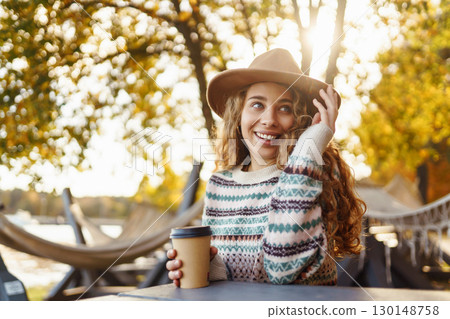 Fall concept woman drinking coffee on bench against backdrop of lake. Enjoying, solitude with nature 130148758