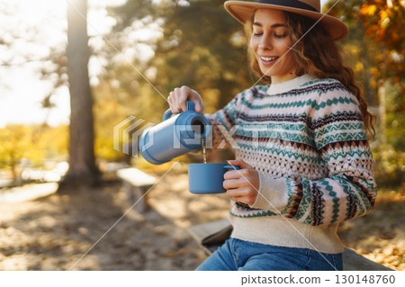 Lady drinks from thermo mug of coffee in nature. Warm up in sunny autumn forest. Travel, adventure. Lady drinks from thermo mug of coffee in nature. Warm up in sunny autumn forest. Travel, adventure. 130148760