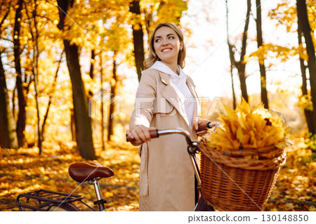 Stylish woman with a bicycle enjoying autumn weather in the park. Beautiful Woman in the autumn forest. 130148850
