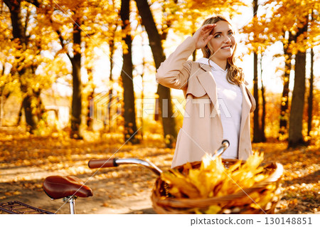 Stylish woman with a bicycle enjoying autumn weather in the park. Beautiful Woman in the autumn forest. Stylish woman with a bicycle enjoying autumn weather in the park. Beautiful Woman in the autumn forest. 130148851