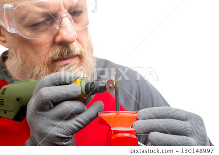 A skilled craftsman in safety goggles focuses intently on a rotary tool as he grinds a metal object A skilled craftsman in safety goggles focuses intently on a rotary tool as he grinds a metal object 130148997