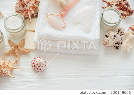 Spa beauty products for body and face home skin care on white wooden background. white towel, bar of soap, jar of cream, pink face roller, wooden brush, and starfish. Self-Care and Beauty concept 130149666