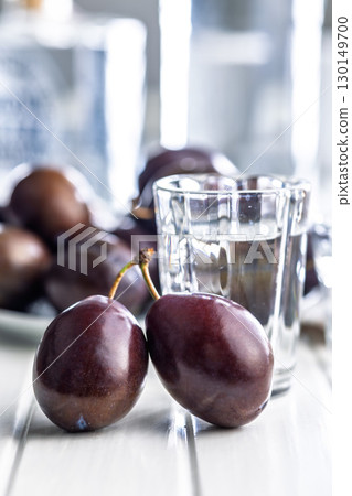 Plums and distilled alcohol on white table. Plum brandy shot. 130149700