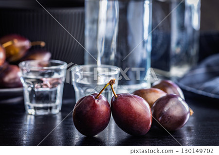 Plums and distilled alcohol on black table. Plum brandy shot. 130149702