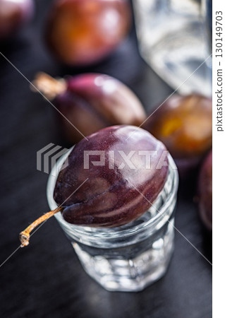 Plums and distilled alcohol on black table. Plum brandy shot. 130149703