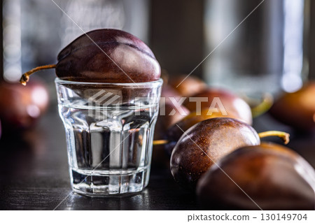 Plums and distilled alcohol on black table. Plum brandy shot. 130149704