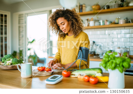 A woman is preparing food in a kitchen with a blood pressure monitor on her arm 130150635