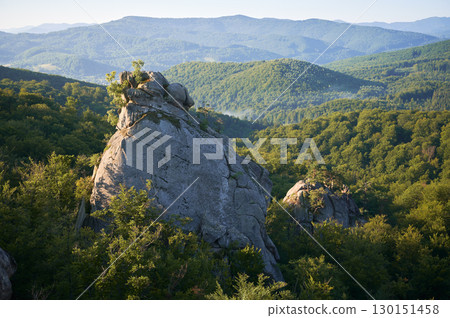 Beautiful panorama of mountain rock surrounded by green foliage with hills and slopes on background Beautiful panorama of mountain rock surrounded by green foliage with hills and slopes on background 130151458