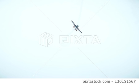 Aerobatic airplane performing at an airshow, flying directly toward the camera with a visible smoke trail in the sky 130151567