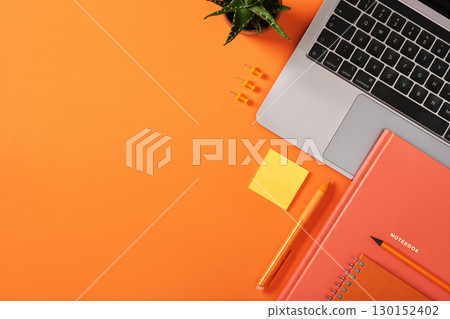 Laptop keyboard with orange stationery, notebook, pen, and sticky note on desk. Workplace with copyspace. 130152402