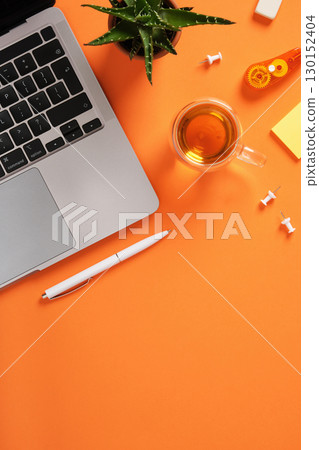 Workspace with laptop keyboard, tea, stationery, and green plant on bright orange desk. Place for text. Workspace with laptop keyboard, tea, stationery, and green plant on bright orange desk. Place for text. 130152404