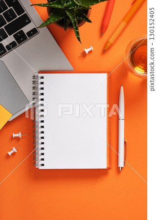 Blank notebook with laptop keyboard, pens, and cup of tea on orange desk. Workspace for study, planning, and creativity. Blank notebook with laptop keyboard, pens, and cup of tea on orange desk. Workspace for study, planning, and creativity. 130152405