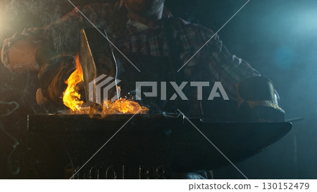 Close-up of blacksmith forging glowing hot iron on anvil with flying sparks 130152479