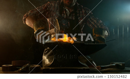 Close-up of blacksmith forging glowing hot iron on anvil with flying sparks Close-up of blacksmith forging glowing hot iron on anvil with flying sparks 130152482