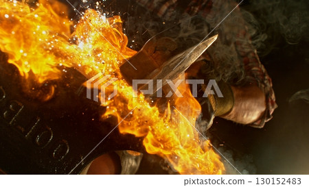 Close-up of blacksmith forging glowing hot iron on anvil with flying sparks 130152483