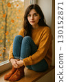 A contemplative woman sitting by a window in autumn 130152871
