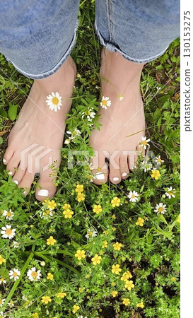 Girl's feet on Green Summer Grass with Field Flowers. Close-up Shot. Summer Time. Bare feet with white pedicures of a young woman. Enjoying the summer time. Girl's feet on Green Summer Grass with Field Flowers. Close-up Shot. Summer Time. Bare feet with white pedicures of a young woman. Enjoying the summer time. 130153275