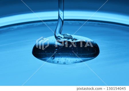 The viscous gel serum for the face flows and collects into a drop on a blue background.. 130154045