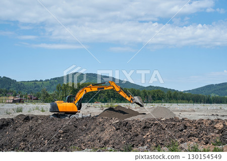 Yellow excavator in action on construction site with dirt pile and scenic 130154549