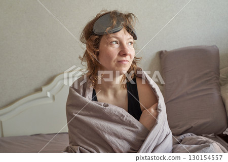 Caucasian female adult relaxing in bed with eye mask and blanket in morning Caucasian female adult relaxing in bed with eye mask and blanket in morning 130154557