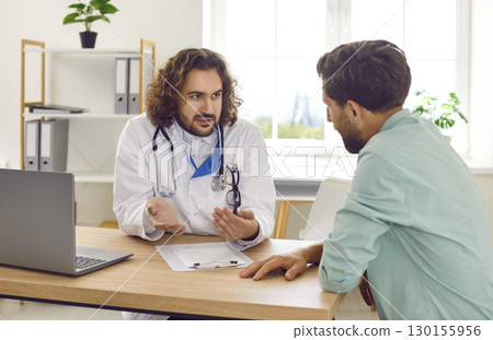 Serious doctor explains benefits of health insurance to patient during clinic meeting. 130155956