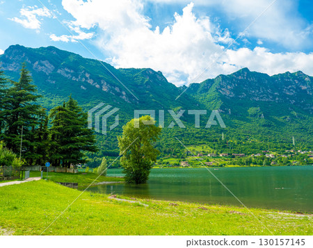 Serene Lake Idro Surrounded by Majestic Mountains and Cloudy sky, Italy, Crone 130157145