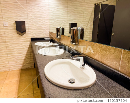 Triple sink counter with mirror and tiled wall in modern restroom. Cleanliness, hygiene, and functional hospitality facility for comfort, order, and guest service. Triple sink counter with mirror and tiled wall in modern restroom. Cleanliness, hygiene, and functional hospitality facility for comfort, order, and guest service. 130157504