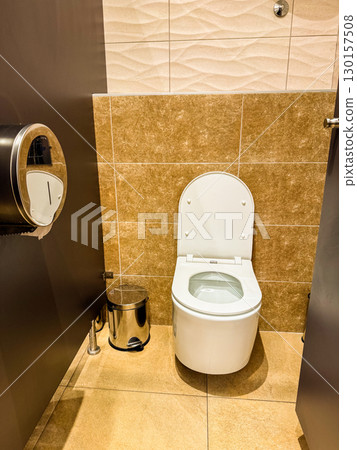 Public restroom interior with toilet and metal bin near tiled wall. Sanitation, hygiene, and facility design for cleanliness, comfort, and guest convenience. Public restroom interior with toilet and metal bin near tiled wall. Sanitation, hygiene, and facility design for cleanliness, comfort, and guest convenience. 130157508
