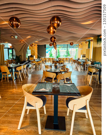 Restaurant with wooden furniture and decorative ceiling lamps. Dining, hospitality, and social interaction concept for leisure, gathering, and culinary experience. 130157509