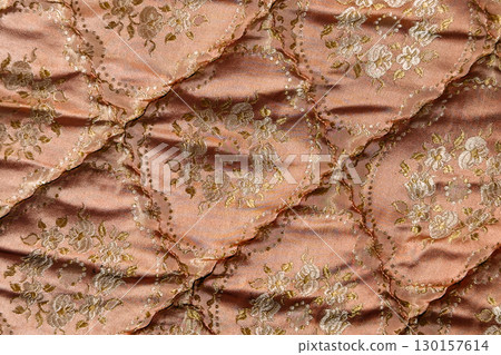 Macro view of vintage quilted fabric with intricate floral embroidery and shimmering pink satin texture. Textile reuse, circular design, upcycled bedding, sustainable sewing Macro view of vintage quilted fabric with intricate floral embroidery and shimmering pink satin texture. Textile reuse, circular design, upcycled bedding, sustainable sewing 130157614